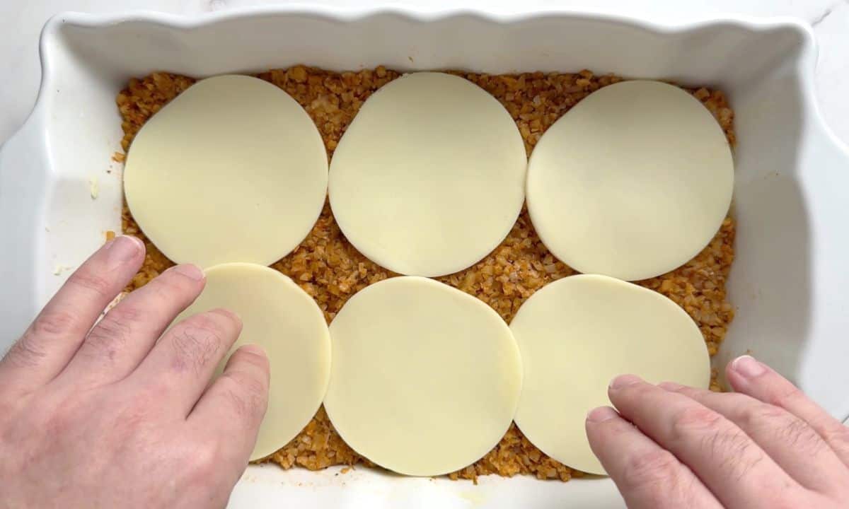 Casserole dish with the cauliflower rice base topped with slices of provolone.