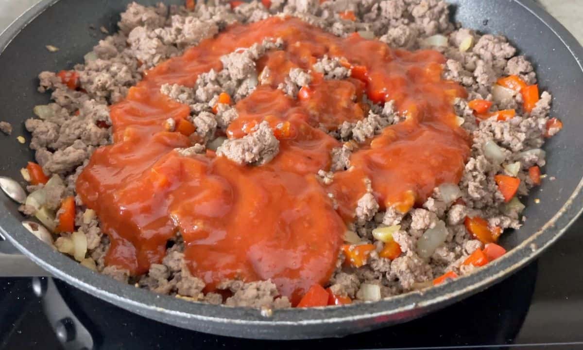 Browning ground beef in a frying pan with added tomato sauce.