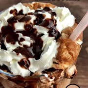 Large glass with sugar free cappuccino topped with whipping cream and chocolate with a plastic straw.