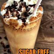 Large glass with sugar free cappuccino topped with whipping cream and chocolate with a plastic straw.