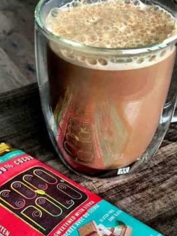 Sugar free spicy hot chocolate in a glass mug next to chocolate bars.