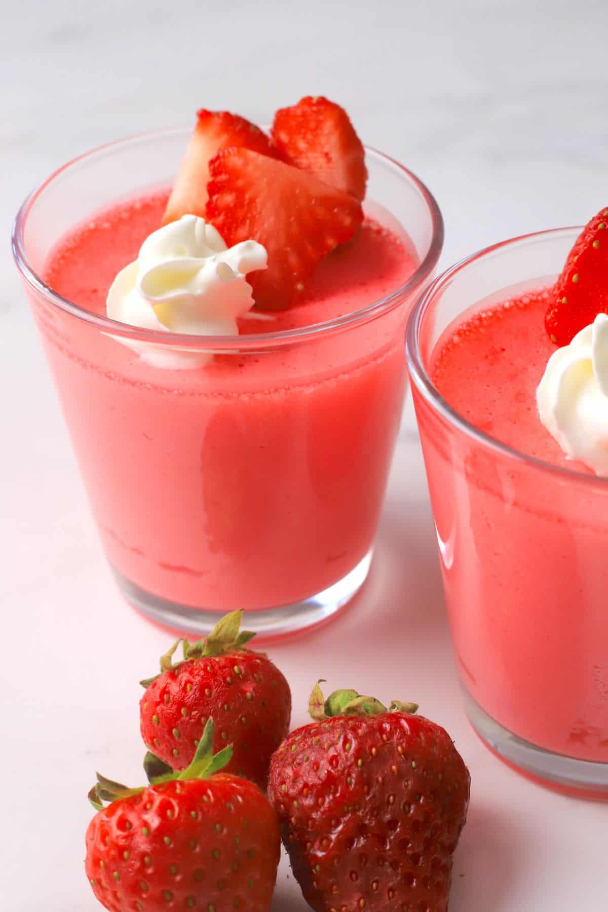 Glass cup with strawberry greek yogurt protein jello topped with strawberries and whipped cream.
