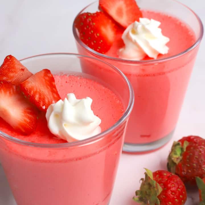 Glass cup with strawberry greek yogurt protein jello topped with strawberries and whipped cream.