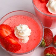 Glass cup with strawberry greek yogurt protein jello topped with strawberries and whipped cream.