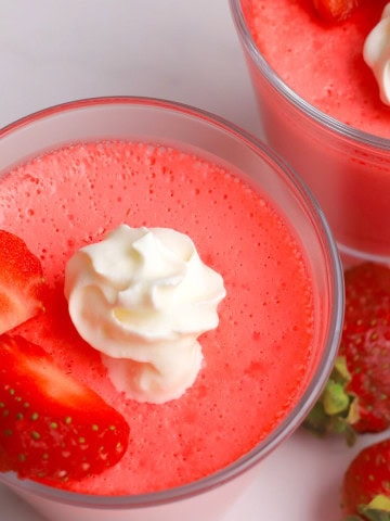 Glass cup with strawberry greek yogurt protein jello topped with strawberries and whipped cream.