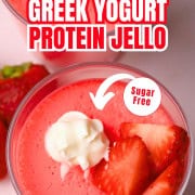 Glass cup with strawberry greek yogurt protein jello topped with strawberries and whipped cream.