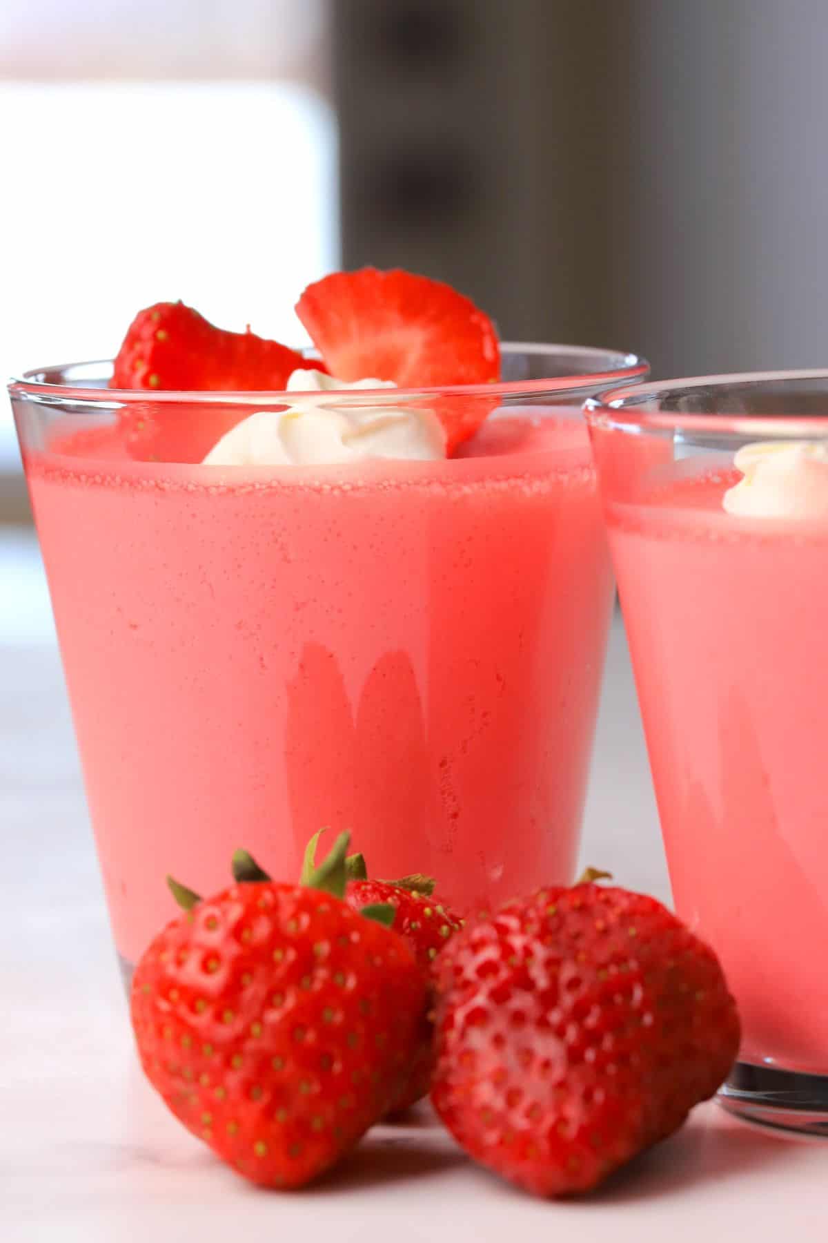 Glass cup with strawberry greek yogurt protein jello topped with strawberries and whipped cream.