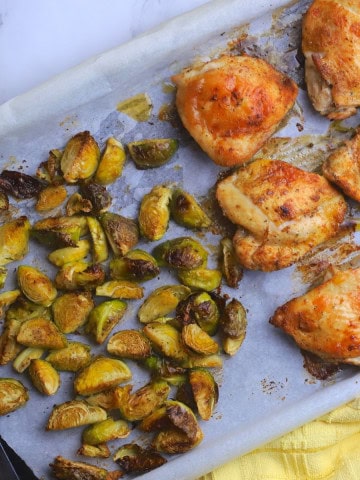 Low carb baked chicken thighs with roasted brussels sprouts on a parchment lined sheet pan.