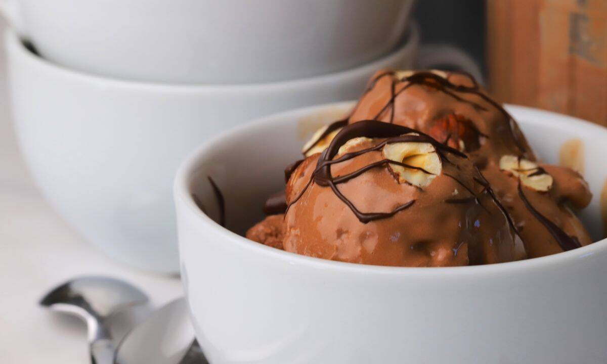 High protein chocolate hazelnut ice cream topped with roasted hazelnuts and chocolate drizzle in a bowl.
