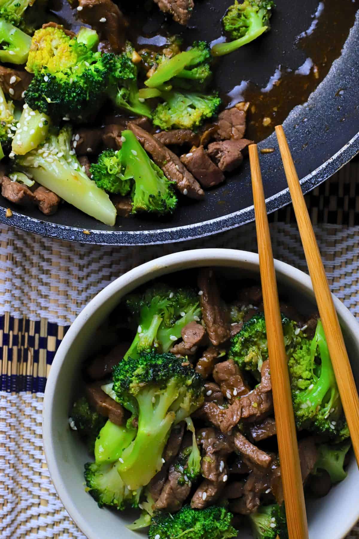 Low carb beef and broccoli in a bowl with chopsticks next to a skillet of the same.