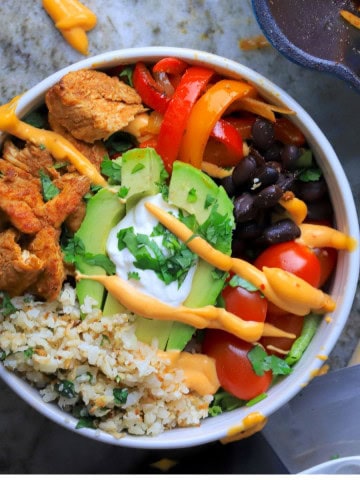 Low carb chicken fajita bowl filled with chicken, peppers, black beans, tomatoes, cauliflower rice and an avocado.