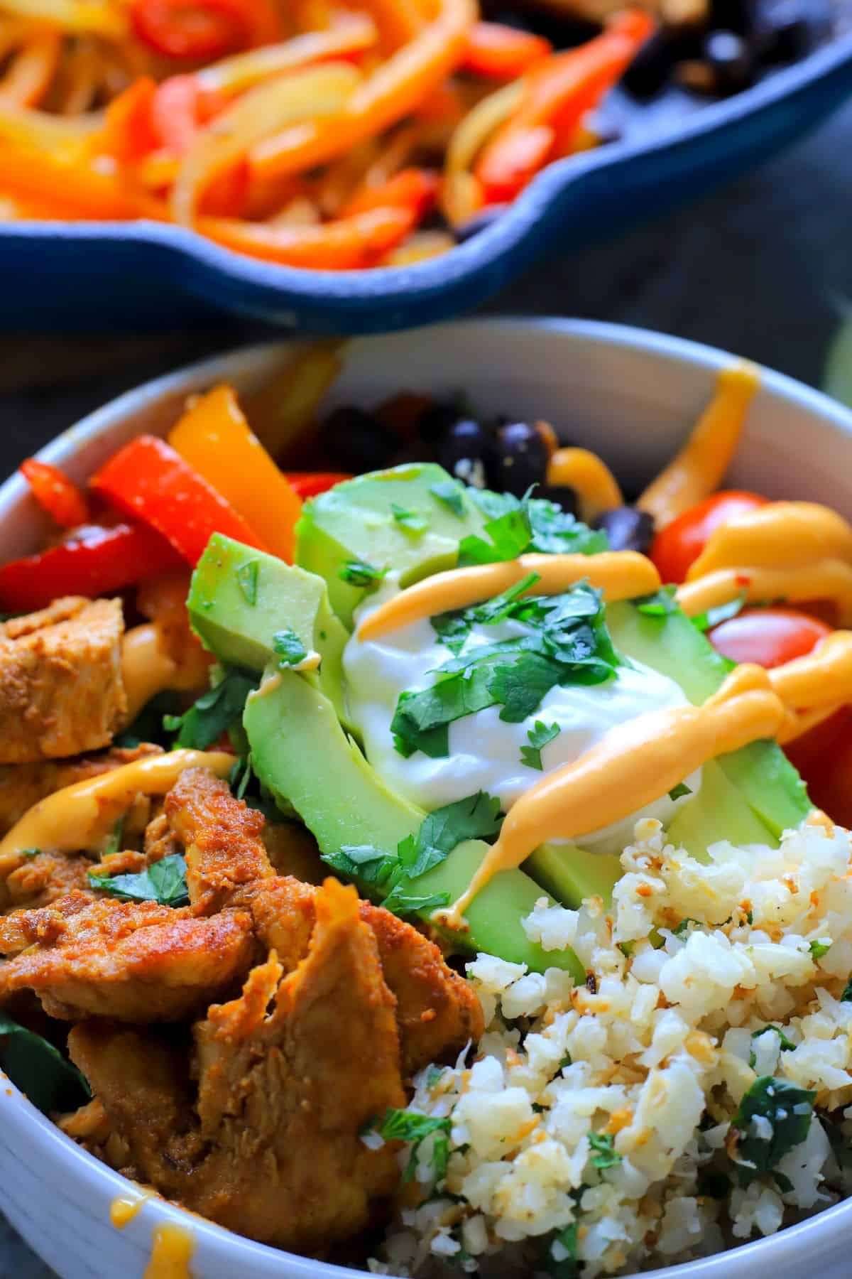 Low carb chicken fajita bowl filled with chicken, peppers, black beans, tomatoes, cauliflower rice and an avocado.