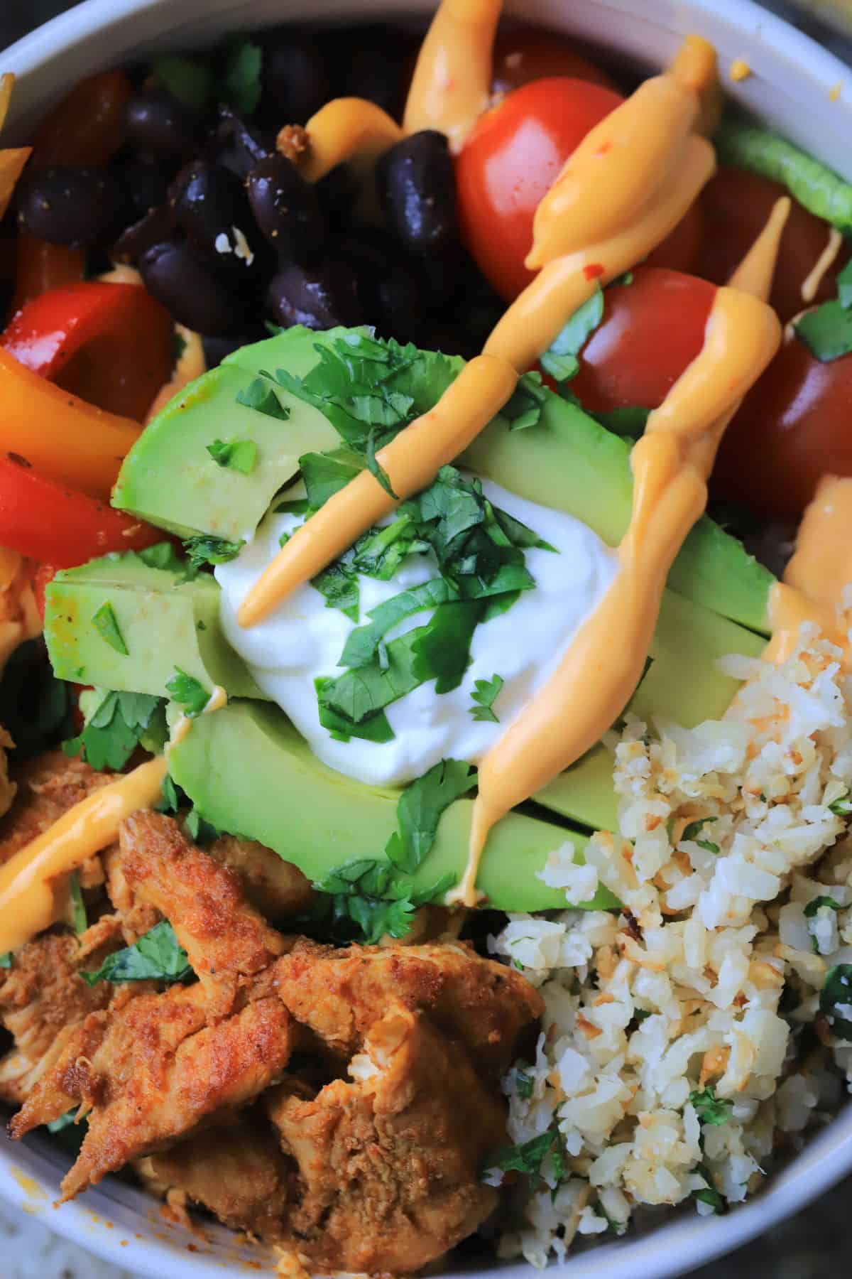 Low carb chicken fajita bowl filled with chicken, peppers, black beans, tomatoes, cauliflower rice and an avocado.