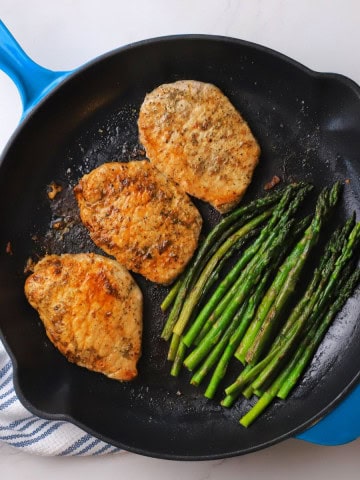 3 pork chops and asparagus in a skillet.