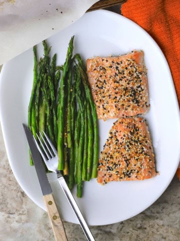 Baked salmon and aspargus on a plate with a knife and a fork.