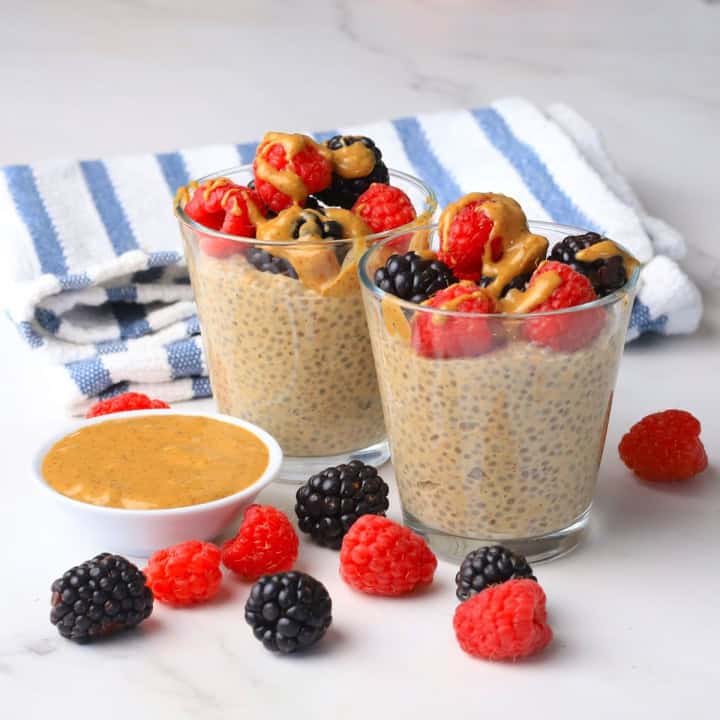 Two cups with low carb chia almond butter pudding topped with berries and almond butter with almond butter and berries on the side.