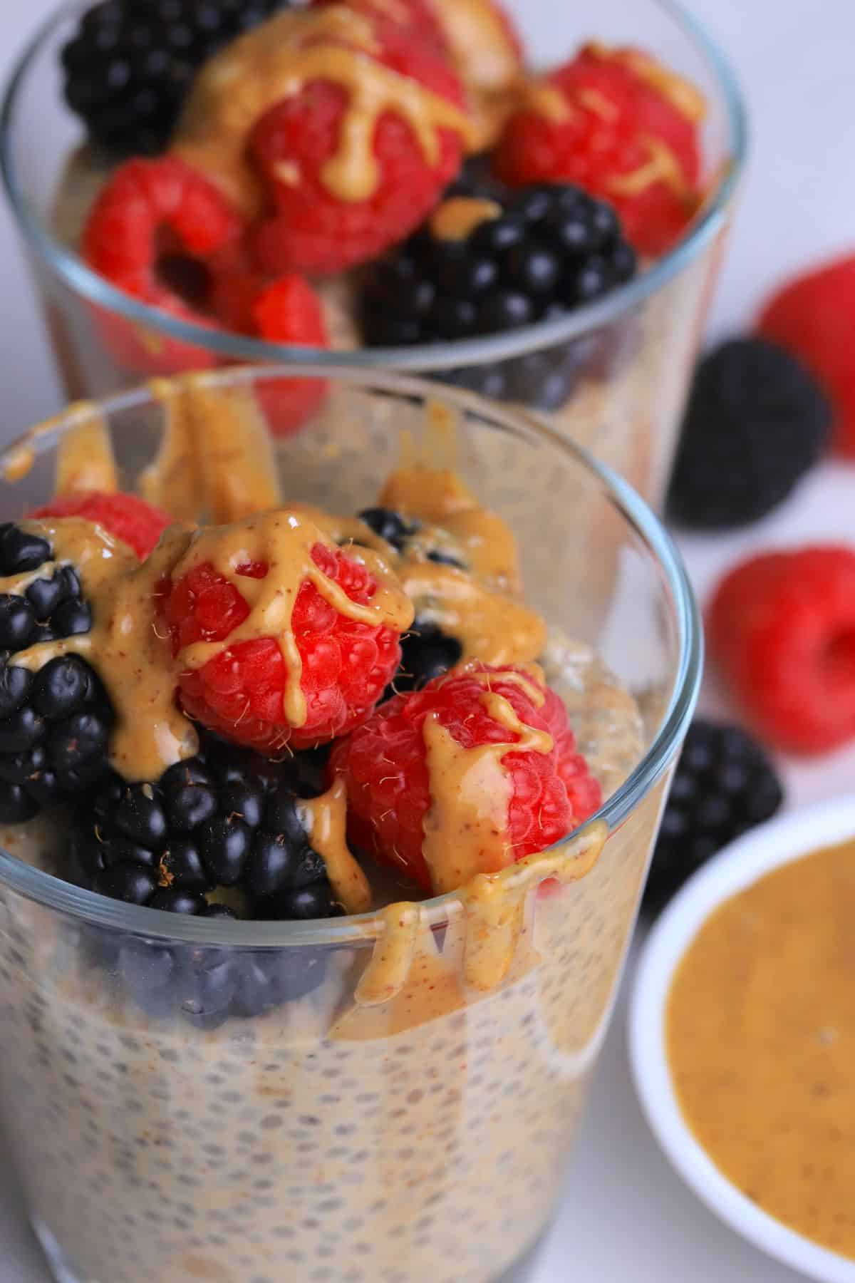 Two cups with low carb chia almond butter pudding topped with berries and almond butter with almond butter and berries on the side.