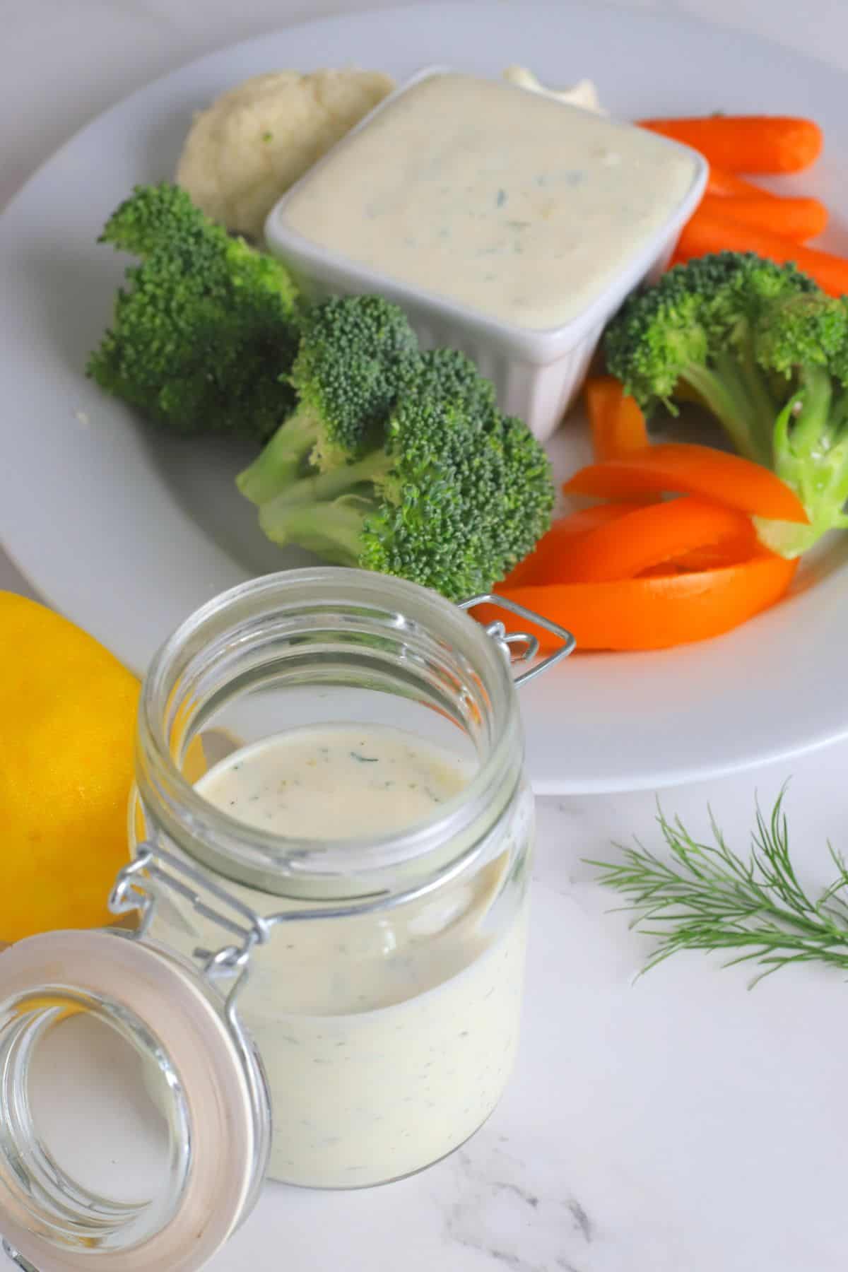Greek yogurt protein ranch in a mason jar next to a plate of vegetables with a ranch dip.