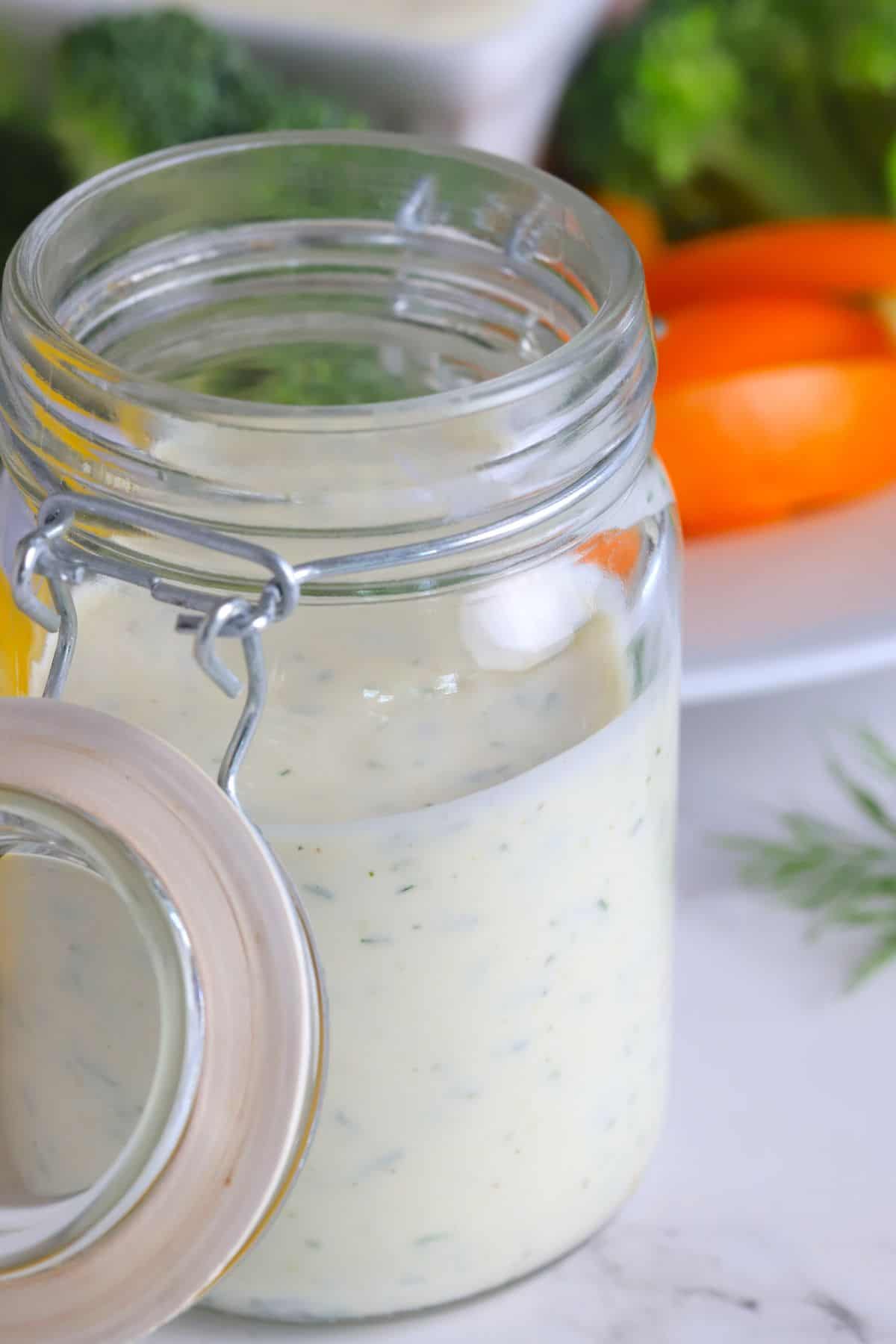 Closeup of Greek yogurt protein ranch in a mason jar next to a plate of vegetables with a ranch dip.