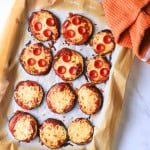 Low carb eggplant pizzas on a parchment lined baking sheet with a an orang dish towel.
