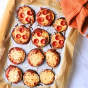 Low carb eggplant pizzas on a parchment lined baking sheet with a an orang dish towel.