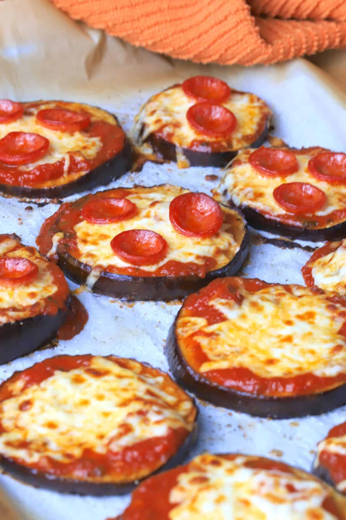 Low carb eggplant pizzas on a parchment lined baking sheet with a dish towel next to it.