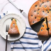 A slice of the low carb ricotta blueberry cake on a plate with a fork, next to the cake.