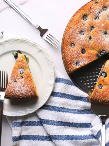 A slice of the low carb ricotta blueberry cake on a plate with a fork, next to the cake.