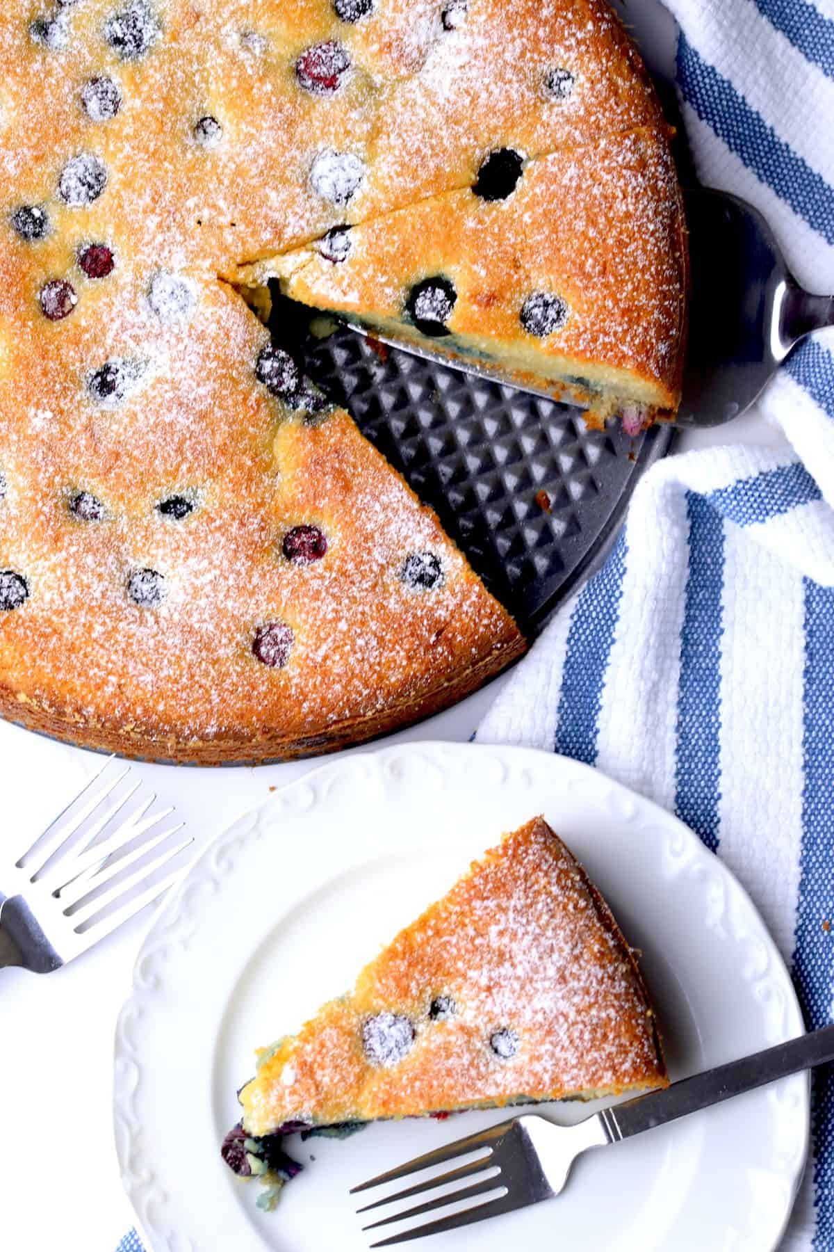 A slice of the low carb ricotta blueberry cake on a plate with a fork, next to the cake.
