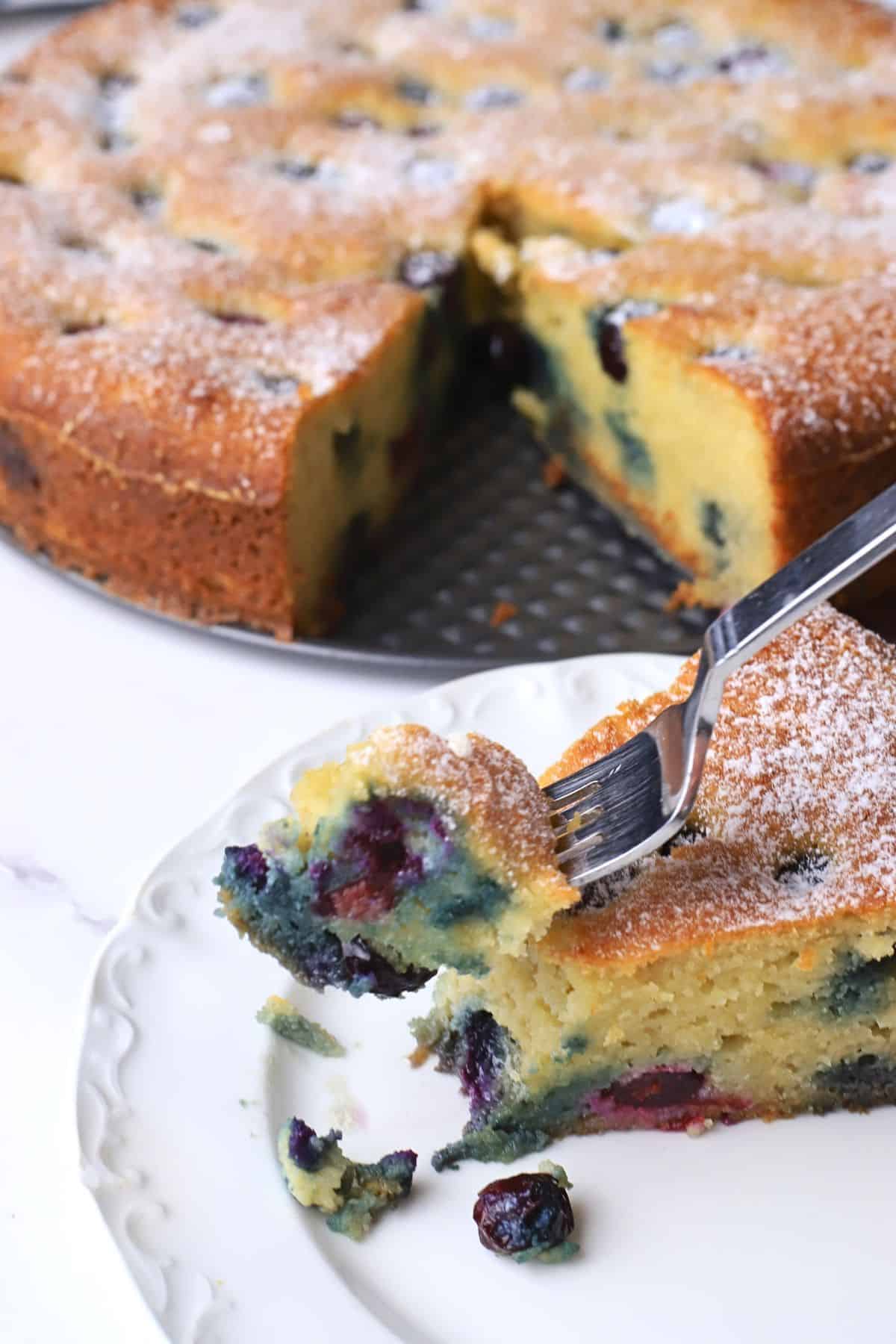 A slice of the low carb ricotta blueberry cake on a plate with a fork, next to the cake.