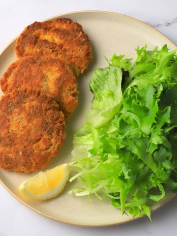 Low carb salmon cakes on a plate with a lemon wedge and a side salad.