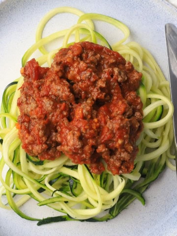 Zucchini noodles on a plate topped with a meat sauce.