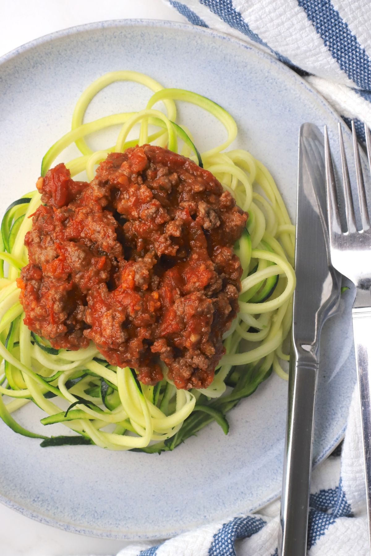Zucchini noodles on a plate topped with a meat sauce.