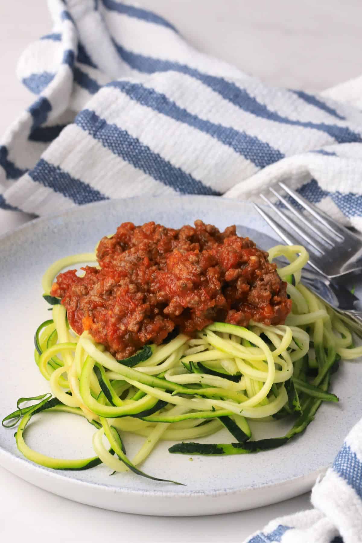 Zucchini noodles on a plate topped with a meat sauce with a napkin.
