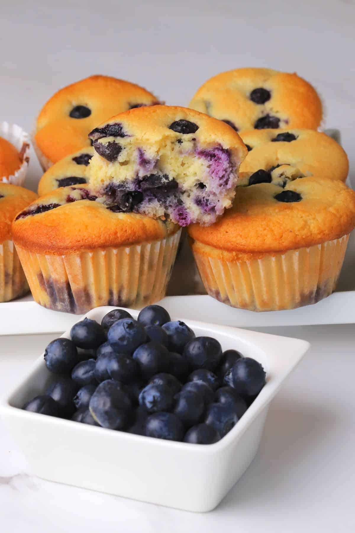 Blueberry cottage cheese muffins next to a bowl of fresh blueberries.