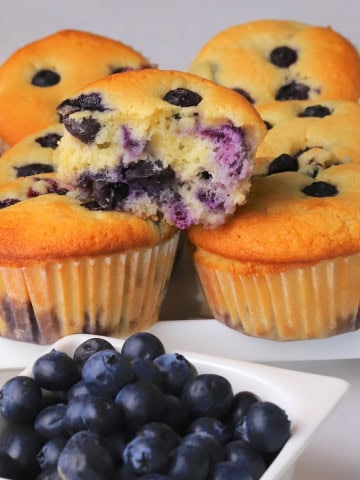Blueberry cottage cheese muffins next to a bowl of fresh blueberries.