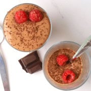 Two high protein cottage cheese dessert chocolate mousse in a glass cup topped with raspberries and chocolate shavings.