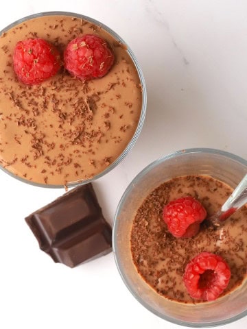 Two high protein cottage cheese dessert chocolate mousse in a glass cup topped with raspberries and chocolate shavings.