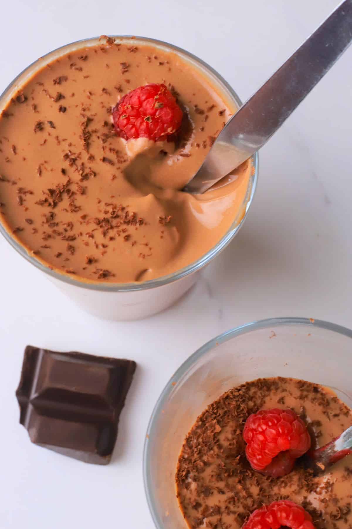 Two high protein cottage cheese dessert chocolate mousse in a glass cup topped with raspberries and chocolate shavings.