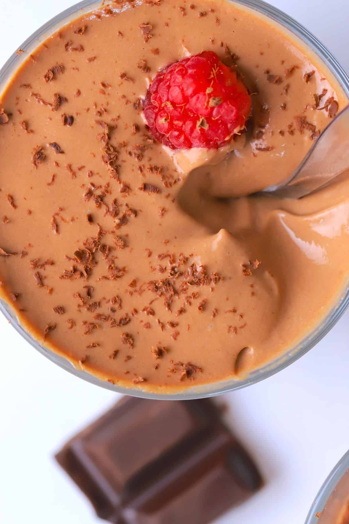 A high protein cottage cheese chocolate mousse dessert in a glass cup topped with raspberries and chocolate shavings.