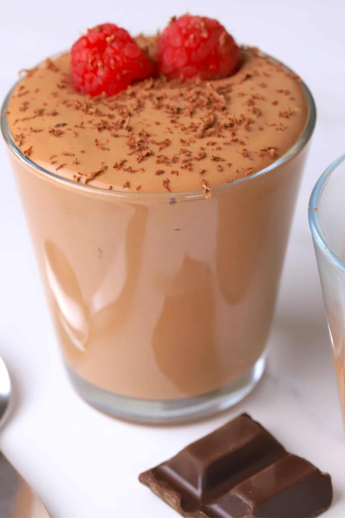 A high protein cottage cheese chocolate mousse dessert in a glass cup topped with raspberries and chocolate shavings.