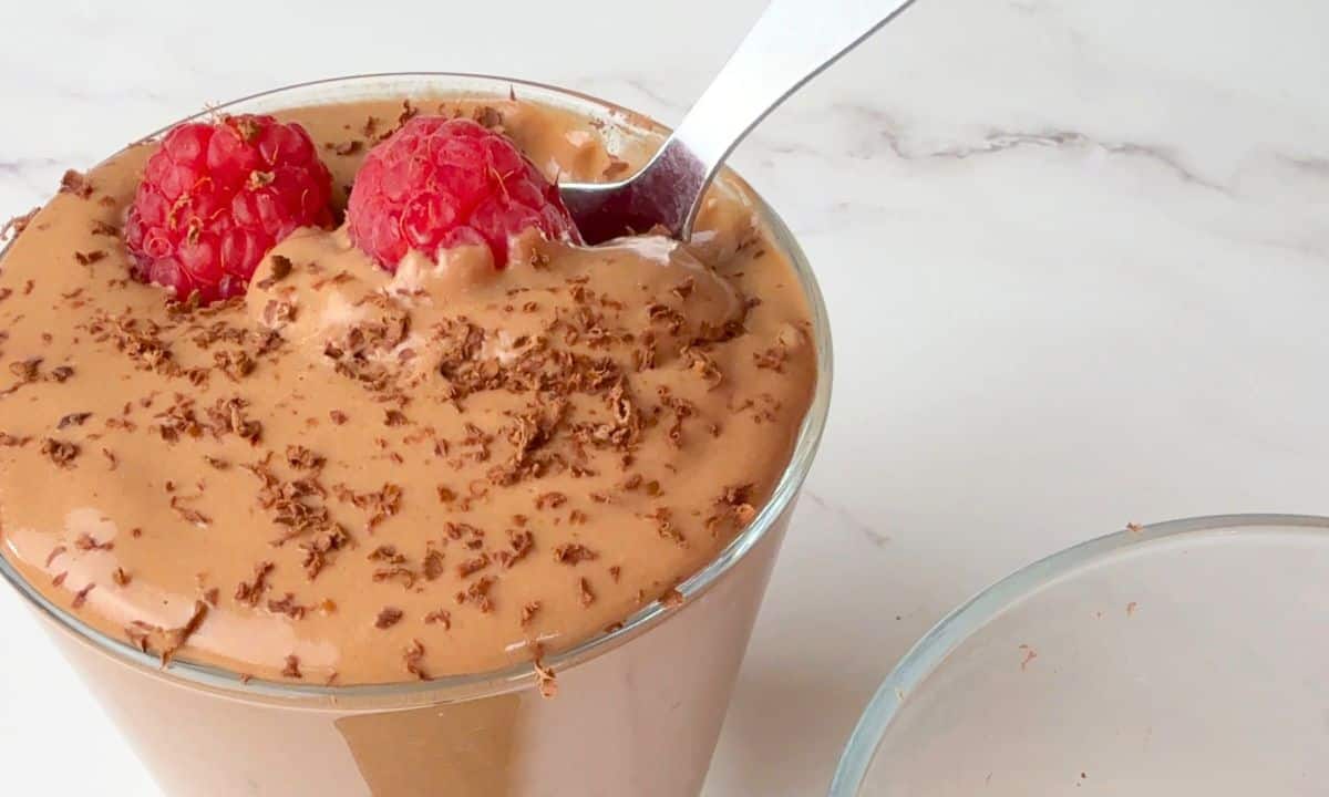Final image of the finished recipe with the chocolate mousse in a glass cup topped with raspberries and chocolate shavings.