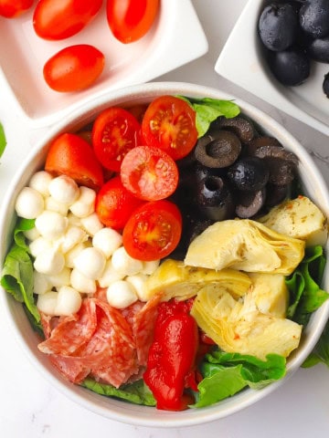 Wide image of the antipasto salad next to a bowl of tomatoes and olives.