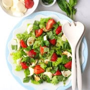 The low carb strawberry caprese salad on a plate next to a bowl of strawberries and basil.