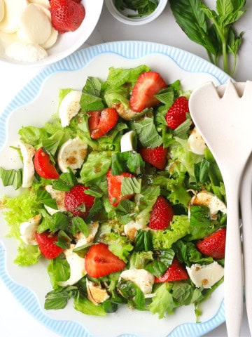 The low carb strawberry caprese salad on a plate next to a bowl of strawberries and basil.