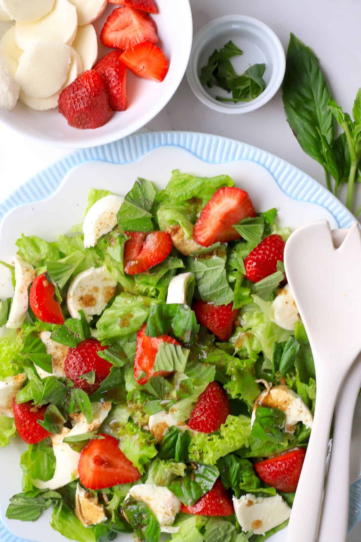 Hero shot of the low carb strawberry caprese salad on a plate next to a bowl of strawberries, cheese and basil.