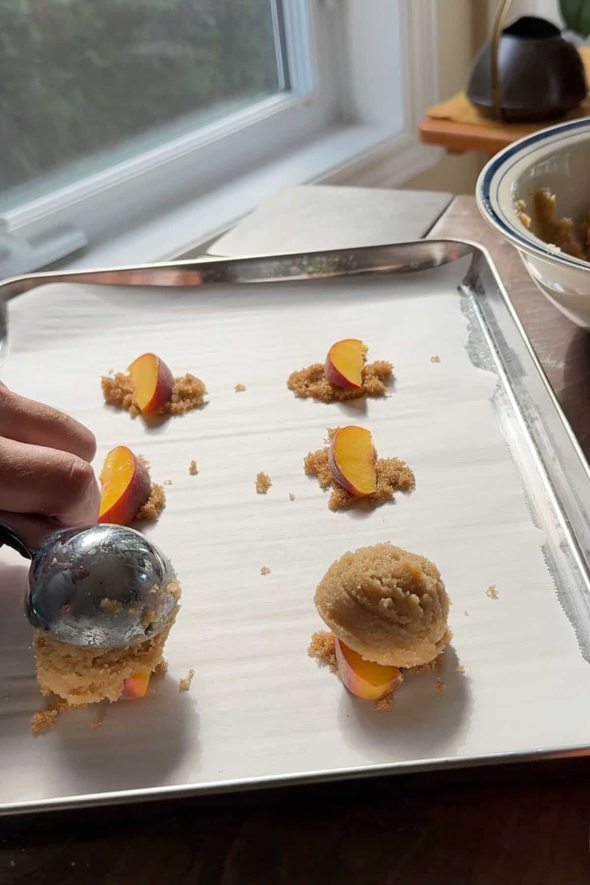 Scooping the cookie dough batter onto the peaches and brown sweetener.