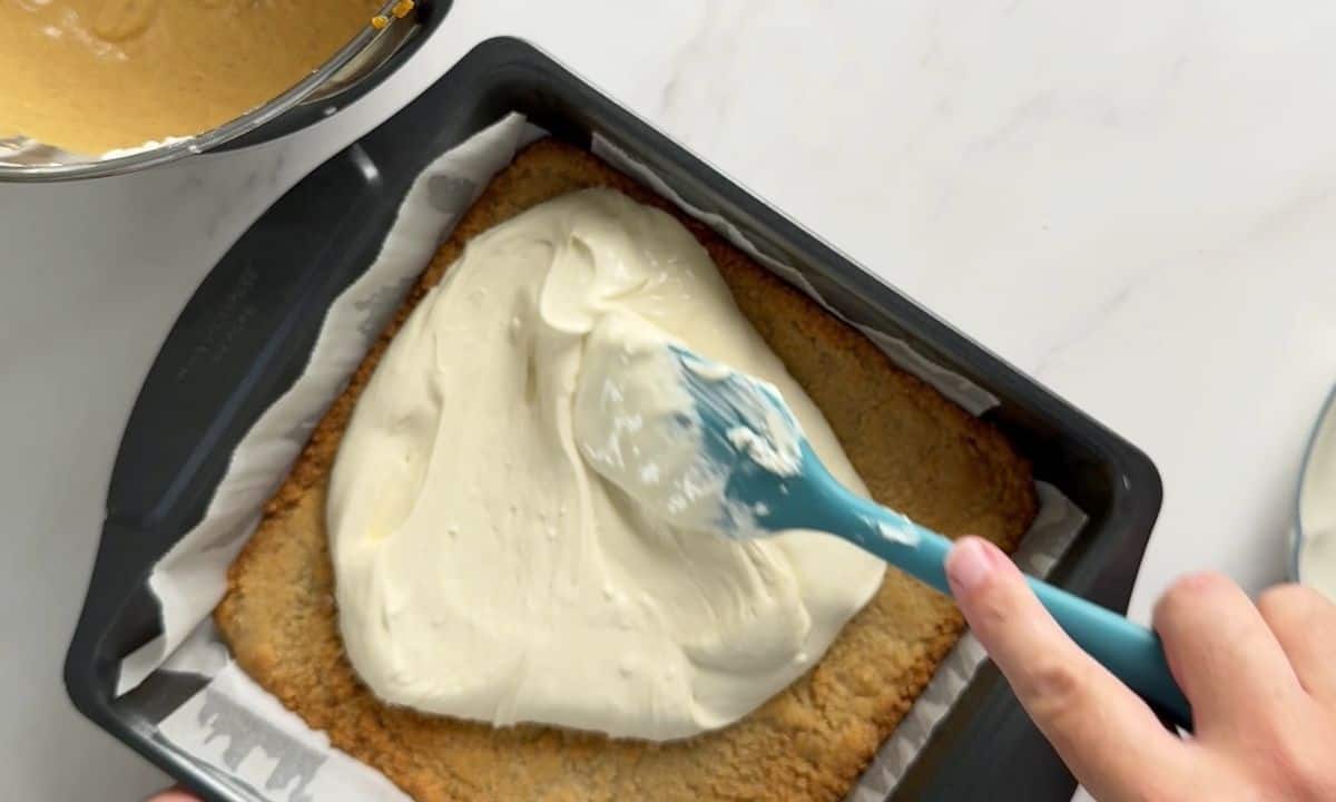 Spreading the cream cheese mixture over the crust in the baking pan.