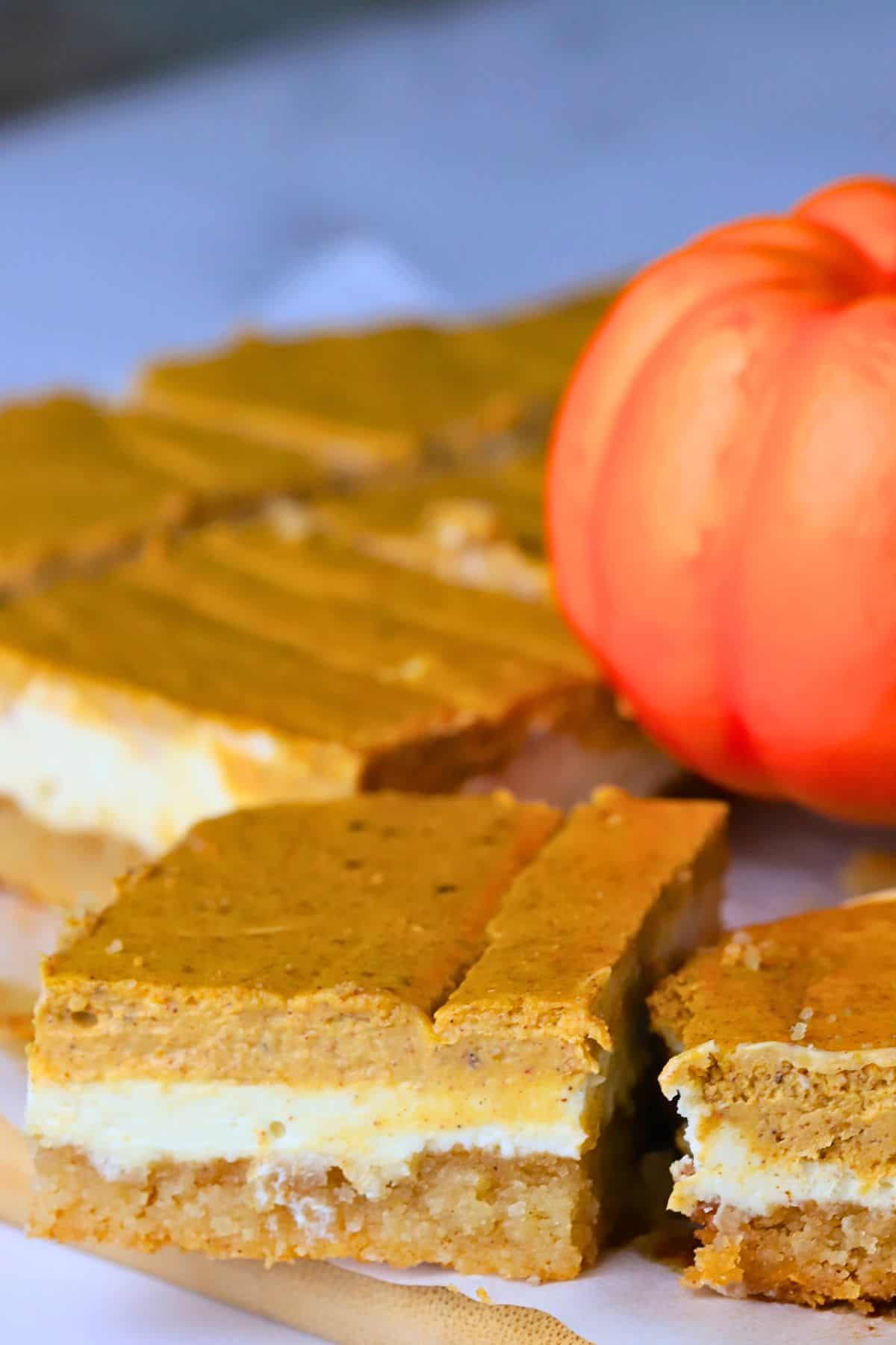 Low carb pumpkin spice cheesecake bars on a cutting board next to a pumpkin.