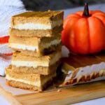 Low carb pumpkin spice cheesecake bars stacked on top of each other next to a pumpkin.